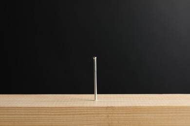 Photo of Metal nail in wooden plank against black background, closeup