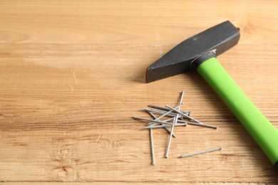 Photo of Metal nails and hammer on wooden table, closeup. Space for text