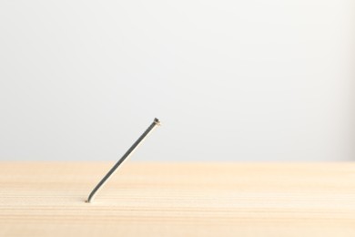 Photo of Metal nail in wooden plank on light grey background, closeup. Space for text