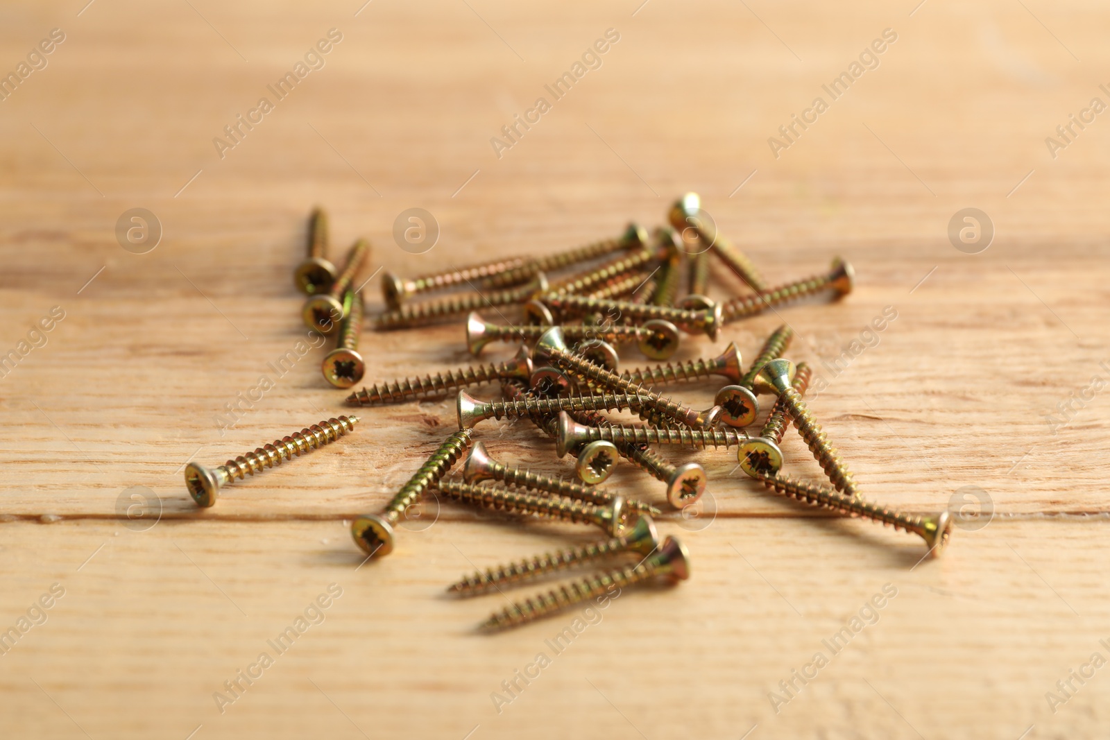 Photo of Many metal screws on wooden table, closeup
