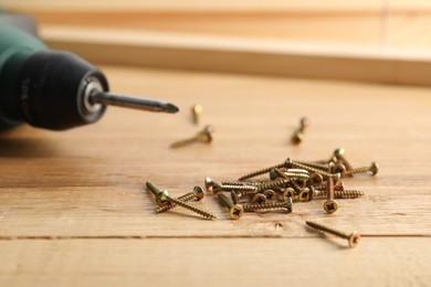Photo of Many metal screws and electric screwdriver on wooden table, closeup