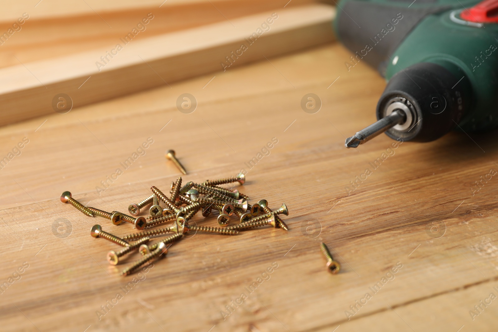 Photo of Many metal screws and electric screwdriver on wooden table, closeup