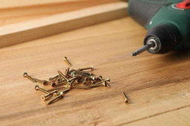 Photo of Many metal screws and electric screwdriver on wooden table, closeup