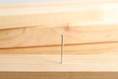 Photo of Metal nail in wooden plank on blurred background, closeup