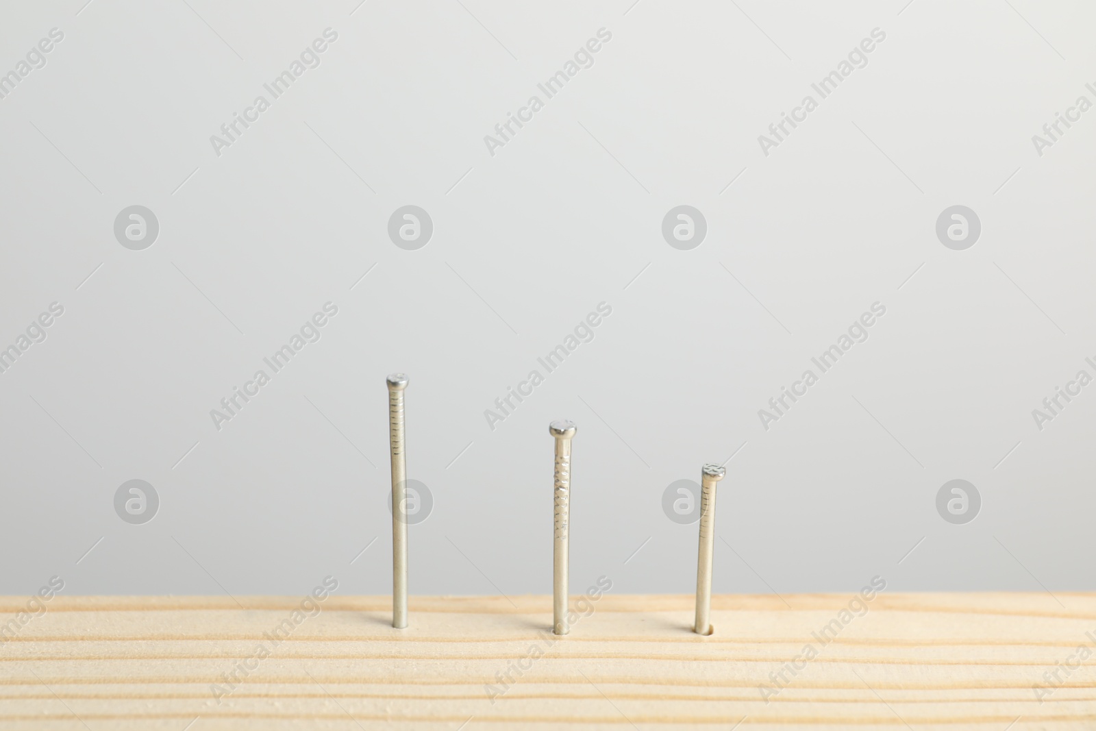 Photo of Metal nails in wooden plank on light grey background, closeup