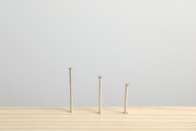 Photo of Metal nails in wooden plank on light grey background, closeup