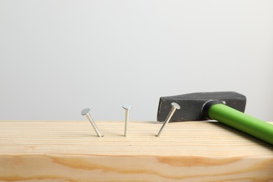 Photo of Metal nails in wooden plank and hammer on light grey background, closeup