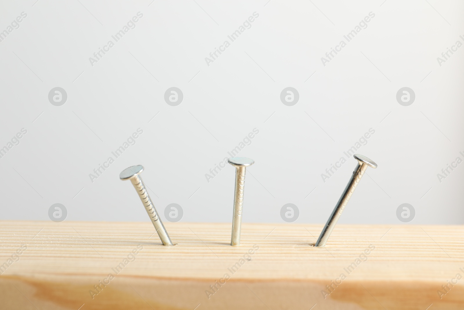 Metal nails in wooden plank on light grey background, closeup Photo of Metal nails in wooden plank on light grey background, closeup