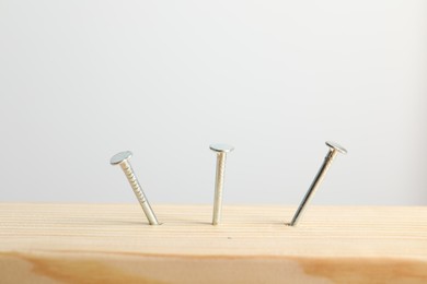 Photo of Metal nails in wooden plank on light grey background, closeup
