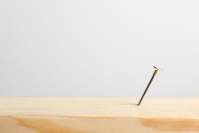 Photo of Metal nail in wooden plank on light grey background, closeup. Space for text