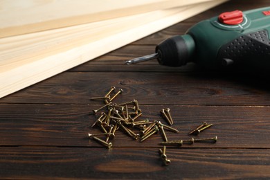 Photo of Screws, planks and electric screwdriver on wooden table, closeup
