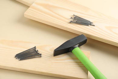 Photo of Metal nails, hammer and wooden planks on beige background, closeup