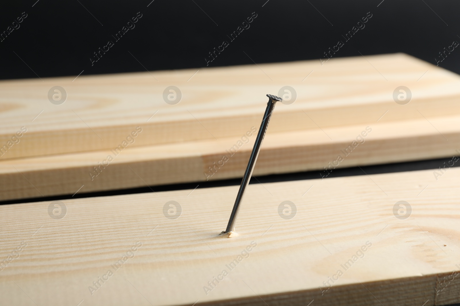 Metal nail in wooden plank on black background, closeup Photo of Metal nail in wooden plank on black background, closeup