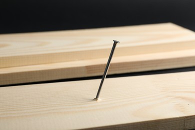 Photo of Metal nail in wooden plank on black background, closeup