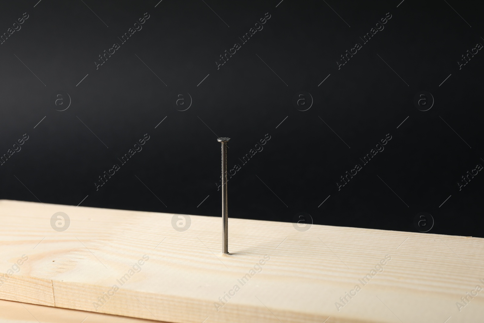 Metal nail in wooden plank on black background, closeup Photo of Metal nail in wooden plank on black background, closeup
