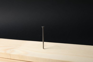 Photo of Metal nail in wooden plank on black background, closeup