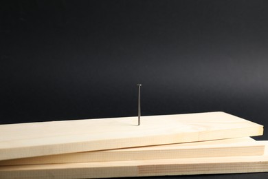 Photo of Metal nail in wooden plank on black background, closeup