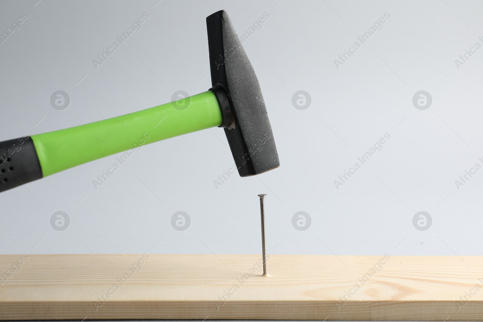 Photo of Hammering nail into wooden plank on light grey background, closeup
