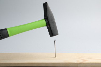 Photo of Hammering nail into wooden plank on light grey background, closeup