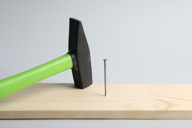 Photo of Metal nail in wooden plank and hammer on light grey background, closeup