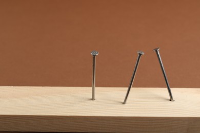 Photo of Metal nails in wooden plank on brown background, closeup. Space for text
