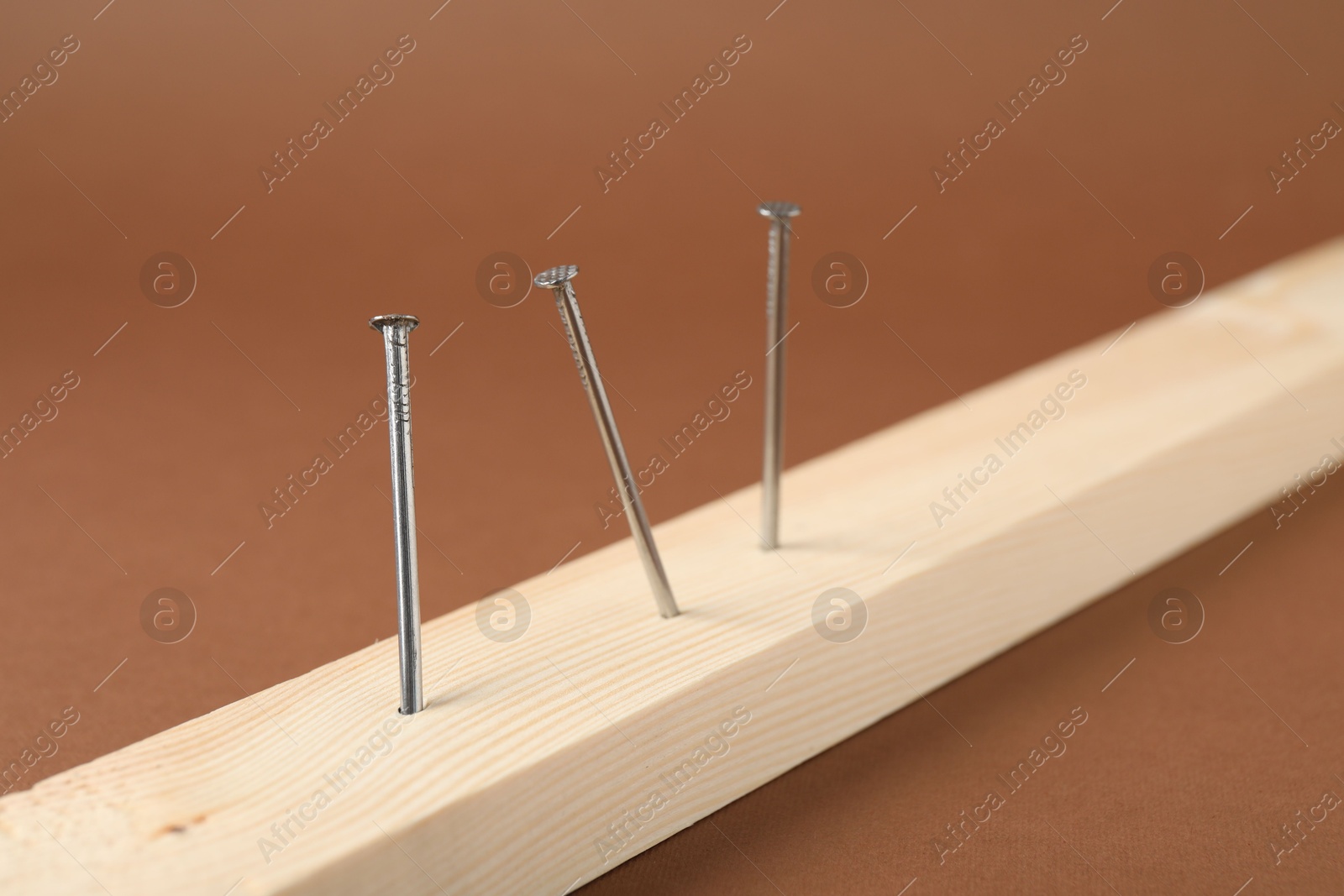 Metal nails in wooden plank on brown background, closeup Photo of Metal nails in wooden plank on brown background, closeup