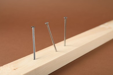 Photo of Metal nails in wooden plank on brown background, closeup