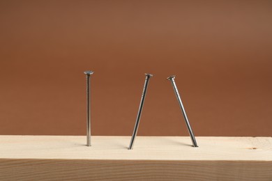 Photo of Metal nails in wooden plank on brown background, closeup
