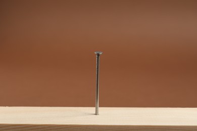 Photo of Metal nail in wooden plank on brown background, closeup