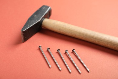 Photo of Metal nails and hammer on coral background, closeup