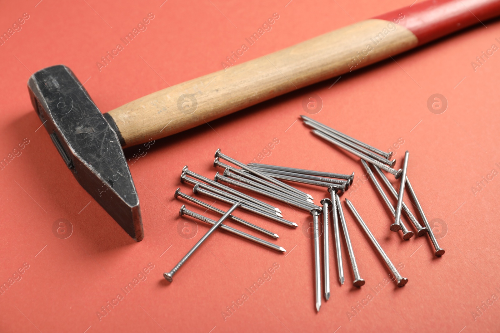 Photo of Metal nails and hammer on coral background, closeup