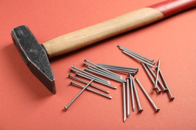 Photo of Metal nails and hammer on coral background, closeup
