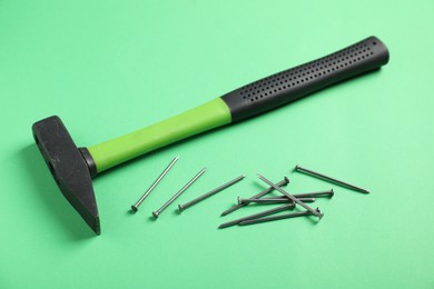 Photo of Metal nails and hammer on green background, closeup