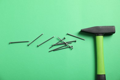 Photo of Metal nails and hammer on green background, flat lay