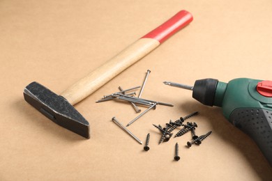 Photo of Metal nails, screws, hammer and electric screwdriver on cardboard surface, closeup