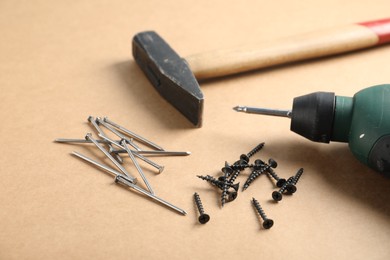 Photo of Metal nails, screws, hammer and electric screwdriver on cardboard surface, closeup
