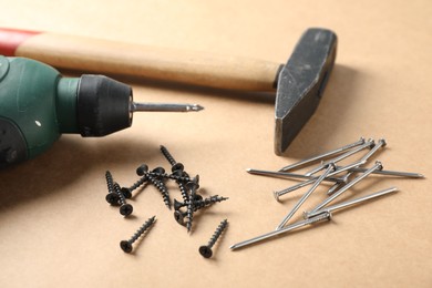 Photo of Metal nails, screws, hammer and electric screwdriver on cardboard surface, closeup