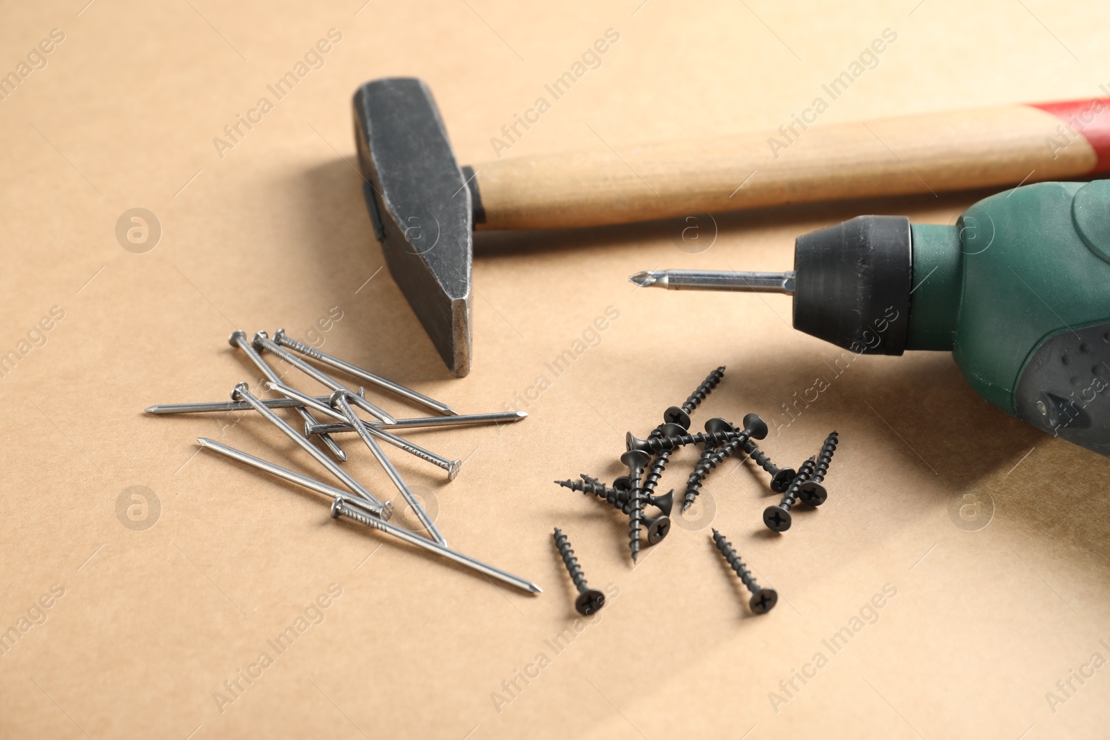 Metal nails, screws, hammer and electric screwdriver on cardboard surface, closeup Photo of Metal nails, screws, hammer and electric screwdriver on cardboard surface, closeup