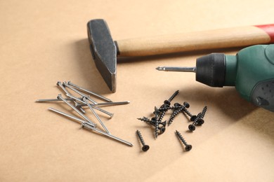 Photo of Metal nails, screws, hammer and electric screwdriver on cardboard surface, closeup