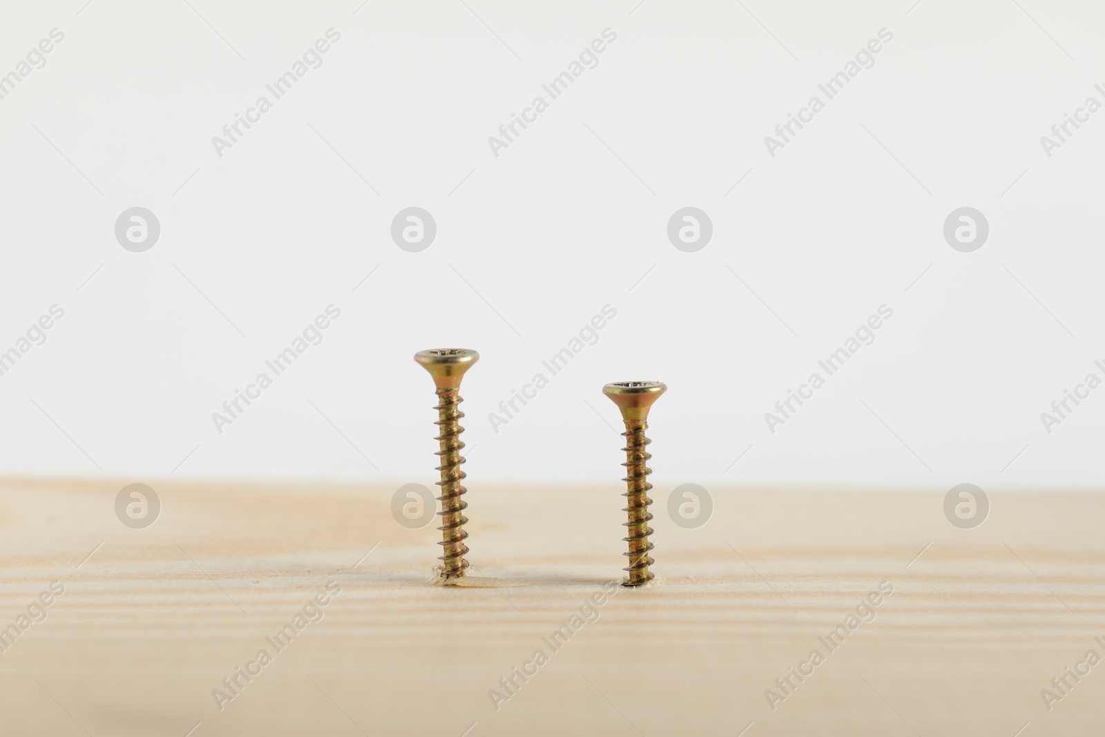 Photo of Metal screws in wooden plank on white background, closeup