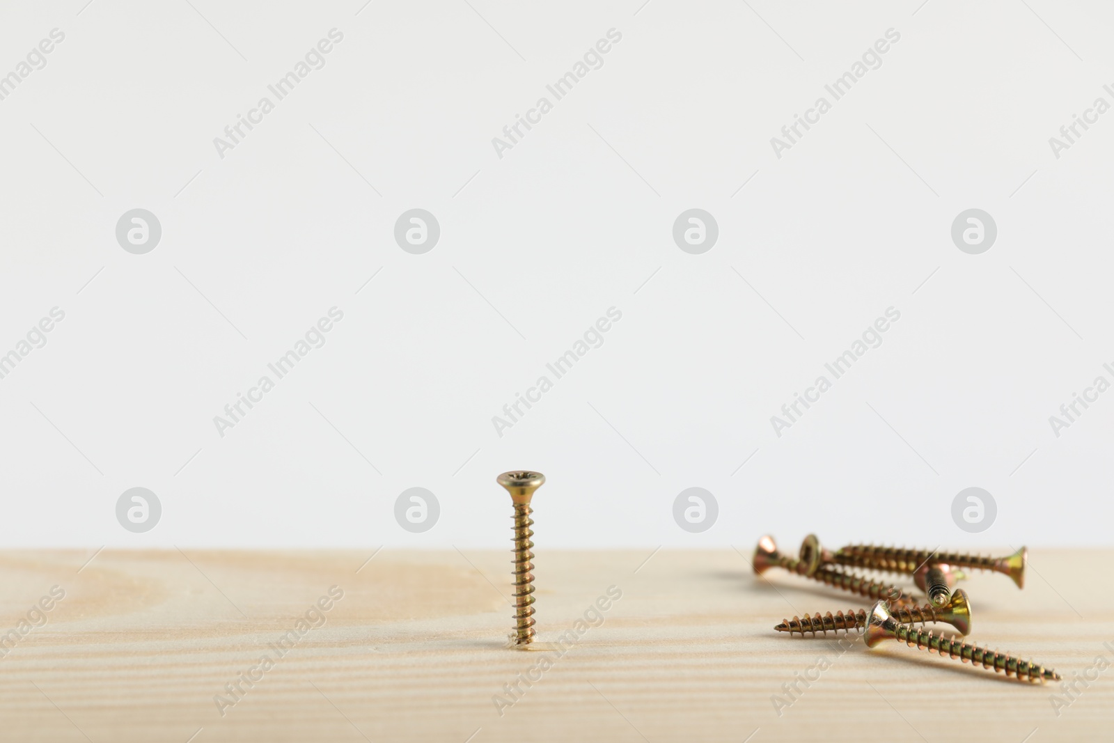 Photo of Metal screws and wooden plank on white background, closeup. Space for text