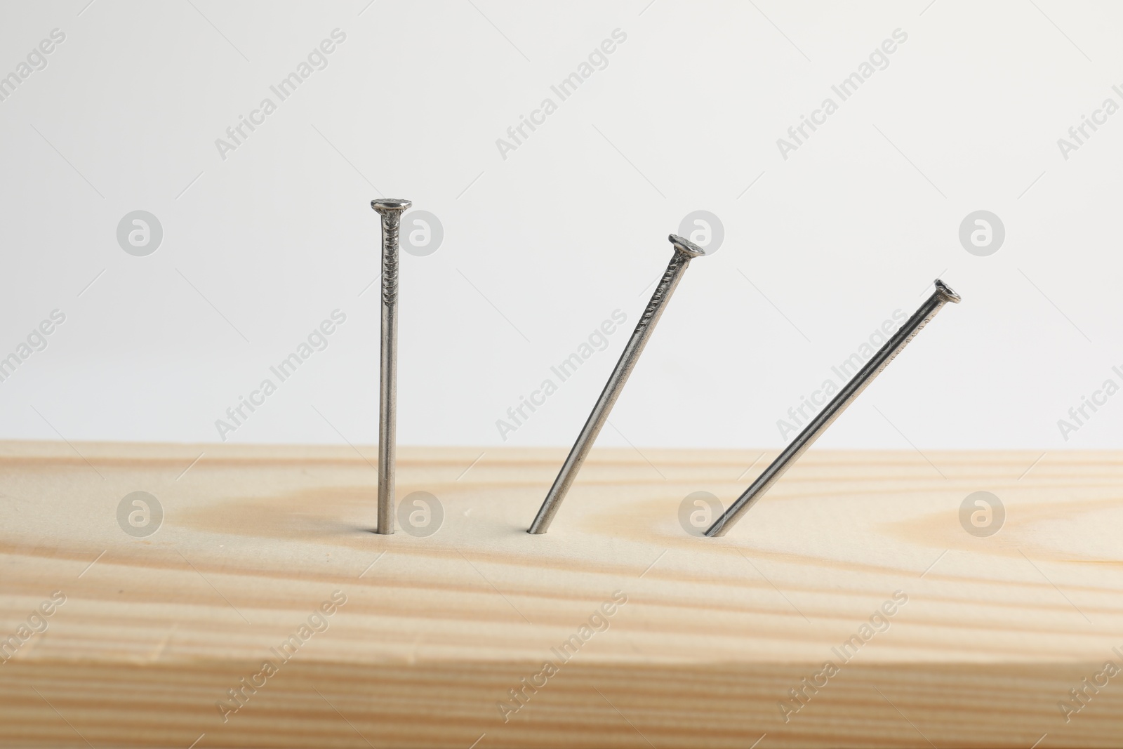 Photo of Metal nails in wooden plank on white background, closeup