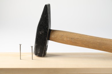 Photo of Metal nails in wooden plank and hammer on white background, closeup