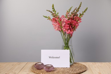 Photo of Card with word Welcome, candles and beautiful flowers on wooden table. Space for text