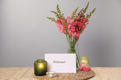 Photo of Card with word Welcome, candles and beautiful flowers on wooden table. Space for text