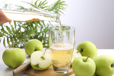 Photo of Woman pouring fresh cider into glass at table, closeup