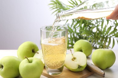 Photo of Woman pouring fresh cider into glass at table, closeup