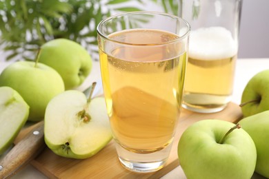 Photo of Fresh cider in glass, bottle, apples and knife on table, closeup