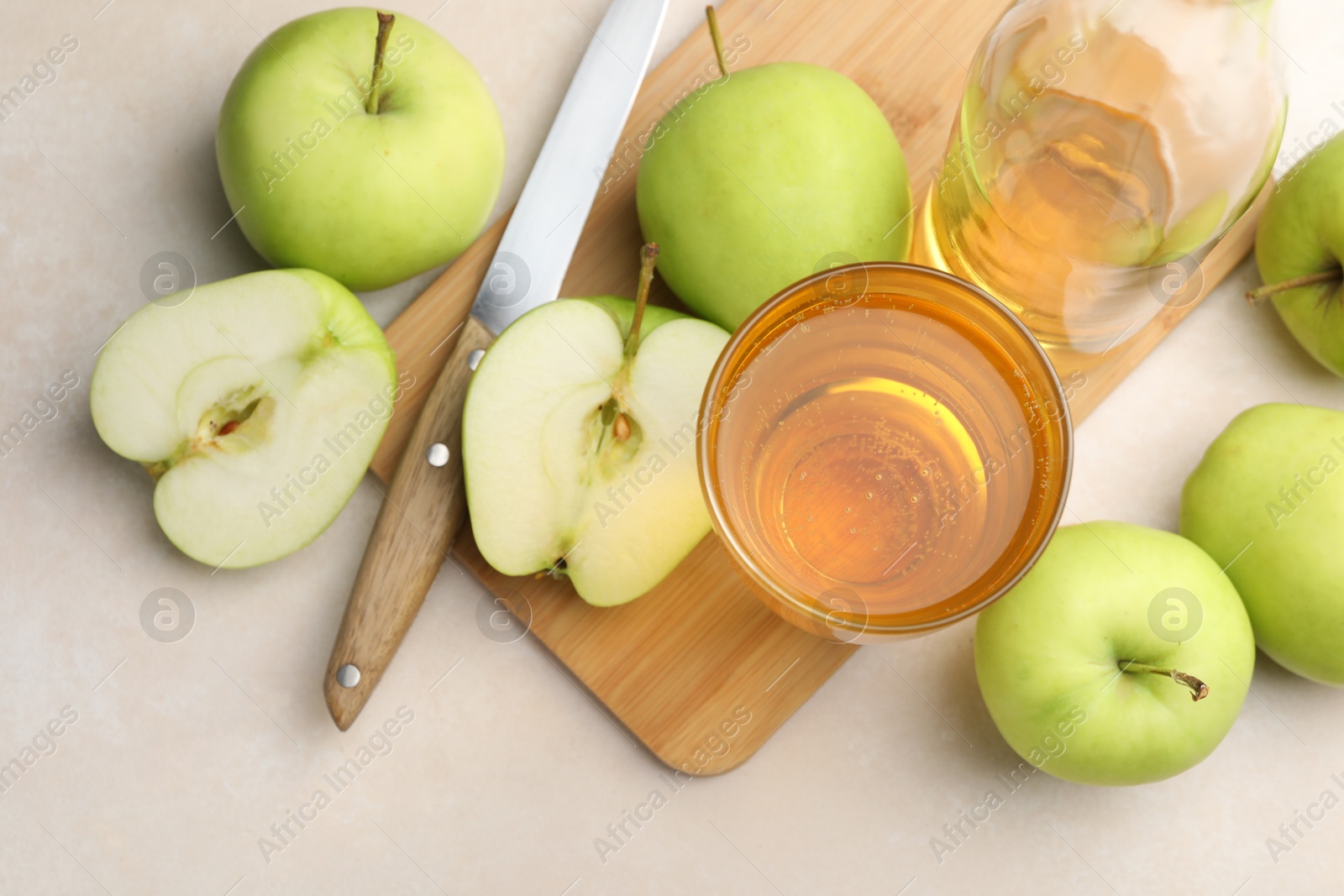 Photo of Fresh cider in glass, bottle, apples and knife on beige table, flat lay