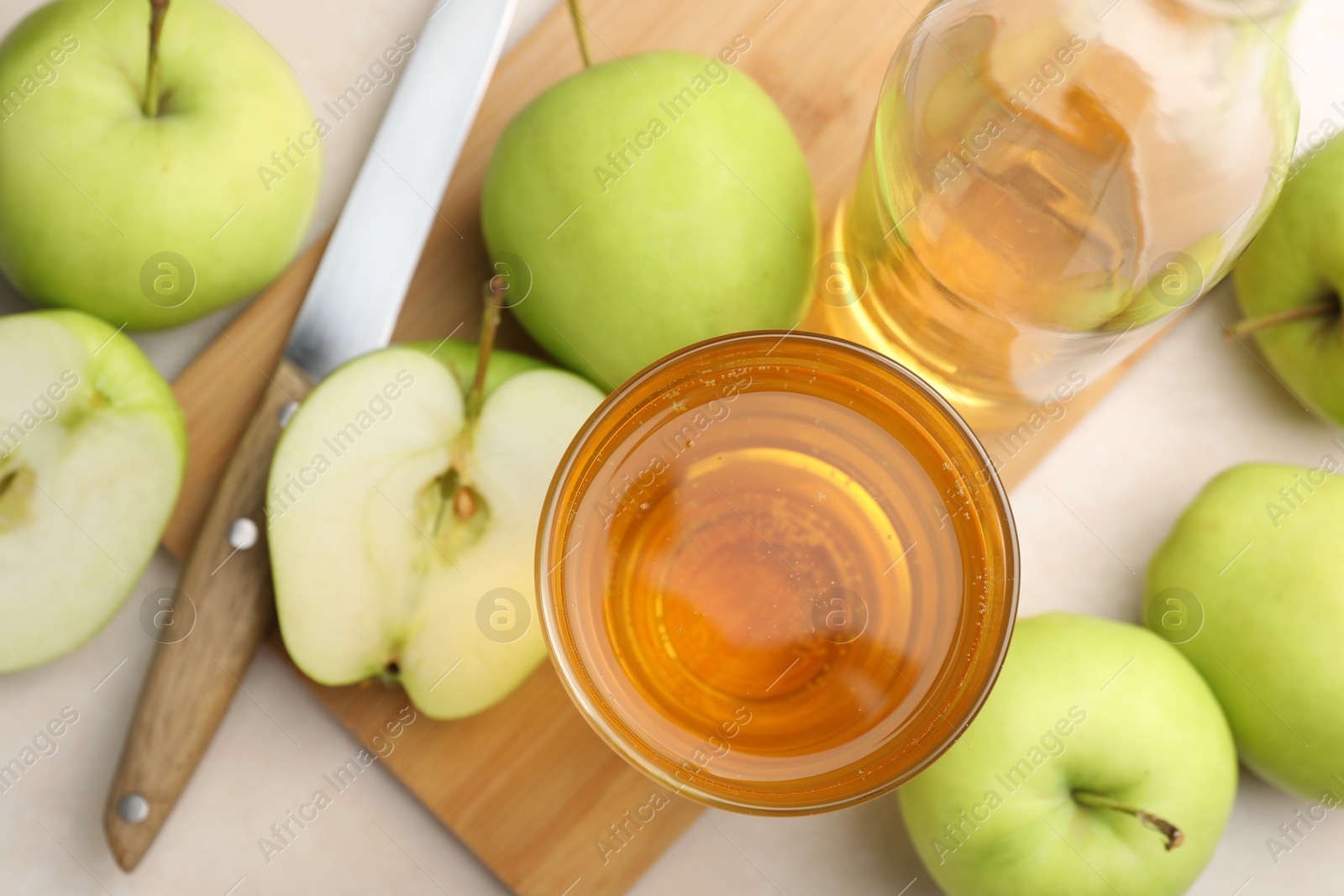 Photo of Fresh cider in glass, bottle, apples and knife on beige table, flat lay